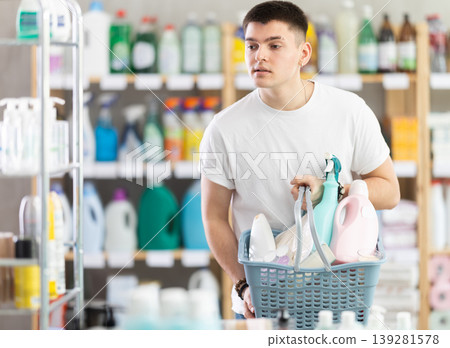 Guy selects various household cleaning products for cleaning the house with full basket of various purchases Guy selects various household cleaning products for cleaning the house with full basket of various purchases 139281578