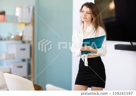 Female coach with folder with papers standing near blackboard in classroom Female coach with folder with papers standing near blackboard in classroom 139281597