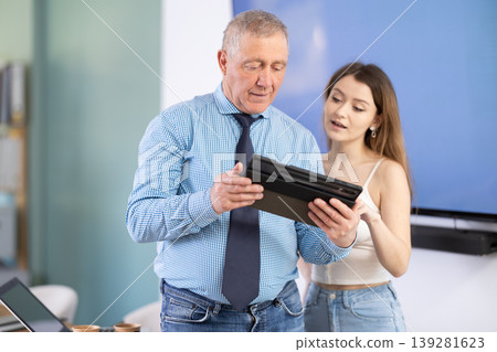 Mature man discussing a new work project with female employee, they look at the tablet Mature man discussing a new work project with female employee, they look at the tablet 139281623