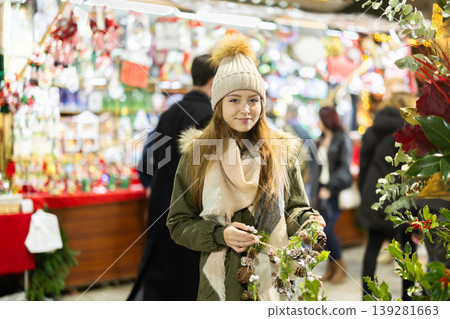 Girl with cone and fir brunch garland stands in middle fair decorated for New Year holidays Girl with cone and fir brunch garland stands in middle fair decorated for New Year holidays 139281663