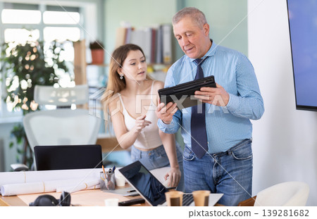 Mature businessman and girl discuss documents on an electronic tablet in company office 139281682