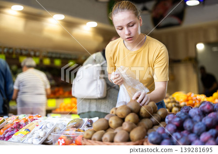 Woman chooses ripe kiwi for purchase in greengrocer shop Woman chooses ripe kiwi for purchase in greengrocer shop 139281695