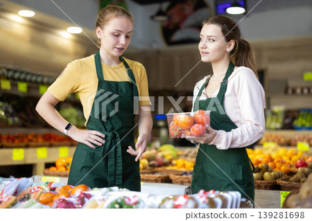 Two female salespeople display persimmons and mangoes in grocery supermarket display case 139281698