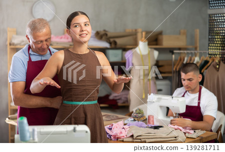 Mature man tailor takes measurements from girl client, guy work with sewing machine Mature man tailor takes measurements from girl client, guy work with sewing machine 139281711