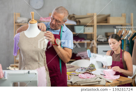 Senior man tailor connects parts of dress on mannequin, girl work and sewing 139281724