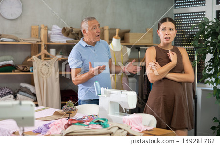 Elderly man scolding young woman in sewing workshop Elderly man scolding young woman in sewing workshop 139281782