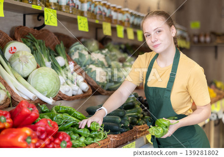 Teenage girl seller puts pepper in vegetable shop Teenage girl seller puts pepper in vegetable shop 139281802