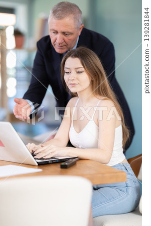 Mature man helps a young woman figure out a laptop Mature man helps a young woman figure out a laptop 139281844