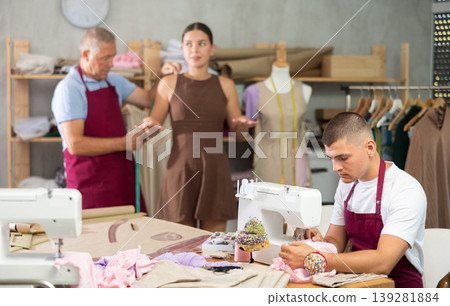 Mature man tailor takes measurements from girl client, guy work with sewing machine Mature man tailor takes measurements from girl client, guy work with sewing machine 139281884