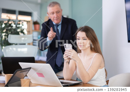 Senior businessman complains to subordinate about her talking on her mobile phone while working in office Senior businessman complains to subordinate about her talking on her mobile phone while working in office 139281945