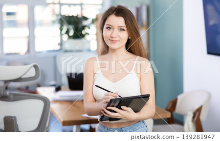 Young woman takes notes on an electronic tablet in modern office interior Young woman takes notes on an electronic tablet in modern office interior 139281947