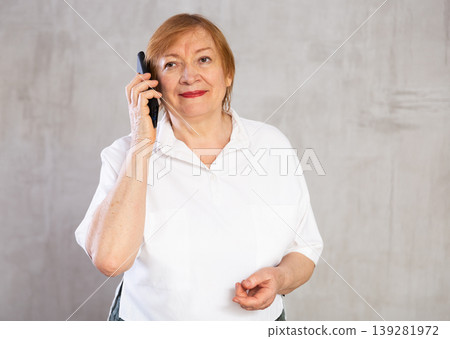 Pensive elderly woman in white shirt talking on mobile phone Pensive elderly woman in white shirt talking on mobile phone 139281972