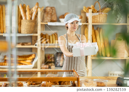 Girl entrepreneur owner of bakery holds out cardboard box with pastries in hand 139282539