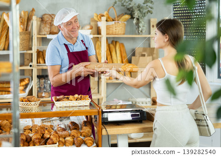 Elderly man seller gives baguette to woman buyer Elderly man seller gives baguette to woman buyer 139282540