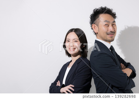 一男一女兩位商務人士背靠背站立，面帶微笑地看向鏡頭，傳遞出信任和團隊合作的形象。 139282698