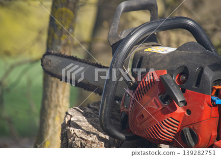 Close-up of a red and black chainsaw resting on a weathered tree stump outdoors Close-up of a red and black chainsaw resting on a weathered tree stump outdoors 139282751