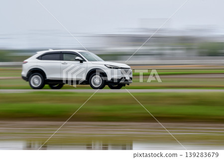 A white SUV speeding through a rural landscape. A white SUV speeding through a rural landscape. 139283679
