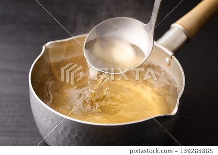 Scoop up the piping hot broth with a ladle. 139283888