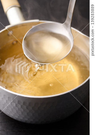 Scoop up the piping hot broth with a ladle. 139283889