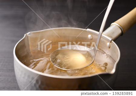 Scoop up the piping hot broth with a ladle. Scoop up the piping hot broth with a ladle. 139283891