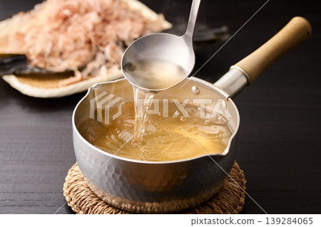 Scoop up the piping hot broth with a ladle. Scoop up the piping hot broth with a ladle. 139284065