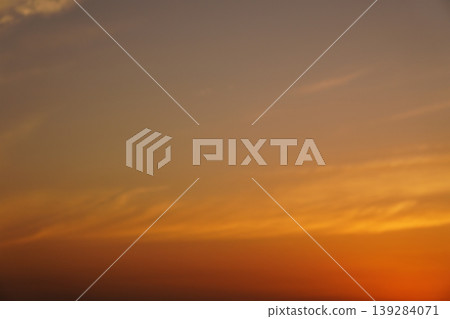 夕陽將天空染成橘色，雲朵緩緩飄過，呈現漸層的效果。 139284071