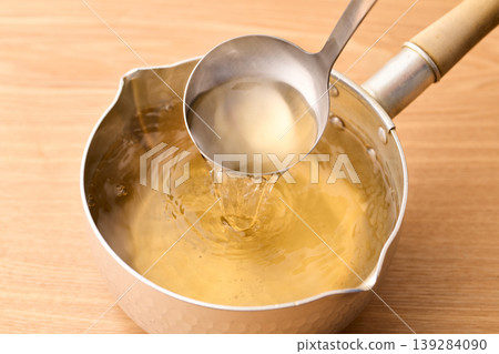 Scoop up the piping hot broth with a ladle. Scoop up the piping hot broth with a ladle. 139284090