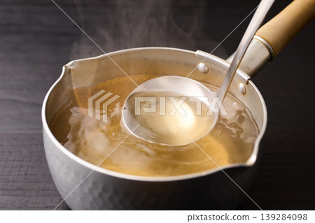 Scoop up the piping hot broth with a ladle. Scoop up the piping hot broth with a ladle. 139284098