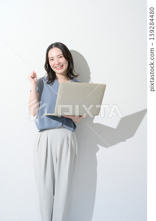 A Japanese woman makes a triumphant gesture while holding a laptop against a white background. A Japanese woman makes a triumphant gesture while holding a laptop against a white background. 139284480