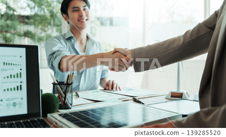 Business meeting handshake across desk in modern office, laptop and financial charts visible, partnership agreement and professional collaboration concept. Business meeting handshake across desk in modern office, laptop and financial charts visible, partnership agreement and professional collaboration concept. 139285520
