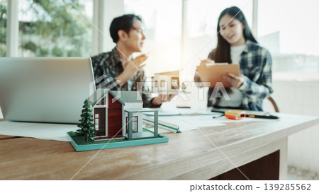 Real estate agents review documents with house model and laptop on desk in bright office, home buying or property investment consultation. Real estate agents review documents with house model and laptop on desk in bright office, home buying or property investment consultation. 139285562