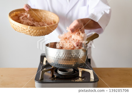 A chef putting bonito flakes into a pot A chef putting bonito flakes into a pot 139285706
