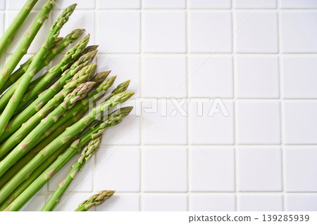 Fresh green asparagus, spring seasonal vegetables arranged on white tiles. Fresh green asparagus, spring seasonal vegetables arranged on white tiles. 139285939