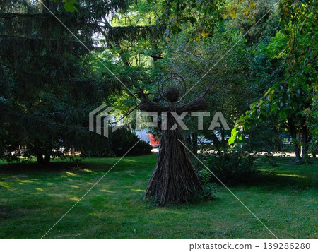 Wicker woman sculpture stands in green grass, surrounded by trees Wicker woman sculpture stands in green grass, surrounded by trees 139286280