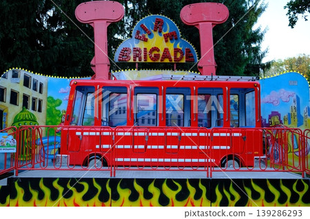 A fairground ride shaped like a red fire truck sits on a platform with painted flames A fairground ride shaped like a red fire truck sits on a platform with painted flames 139286293