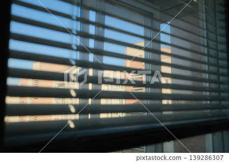 View through blinds shows exterior of building and blue sky, sunny day 139286307