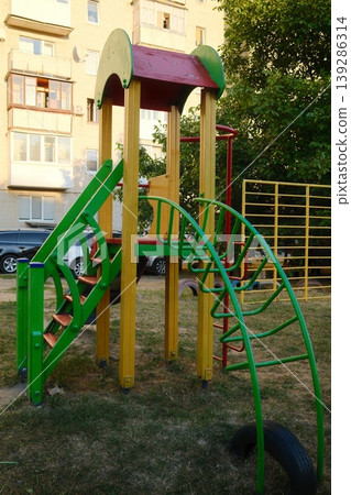 Multi-colored playground with a slide and climbing structure stands on a grassy lawn Multi-colored playground with a slide and climbing structure stands on a grassy lawn 139286314