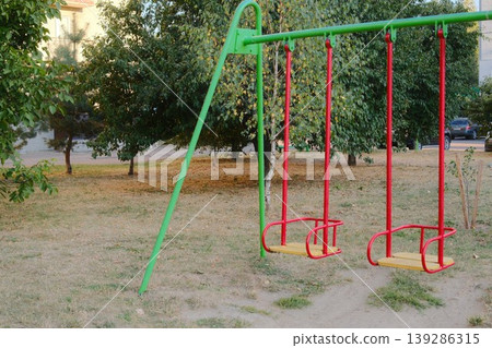 Two swings hang still in a public park setting during daytime Two swings hang still in a public park setting during daytime 139286315
