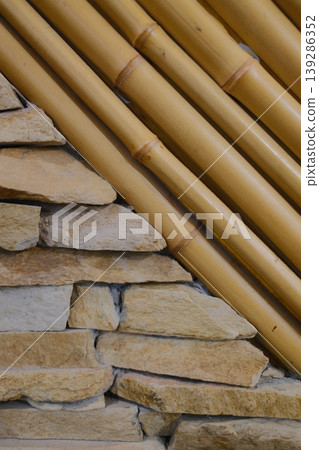 Stacked stones meet parallel bamboo poles at a sharp angle indoors Stacked stones meet parallel bamboo poles at a sharp angle indoors 139286352