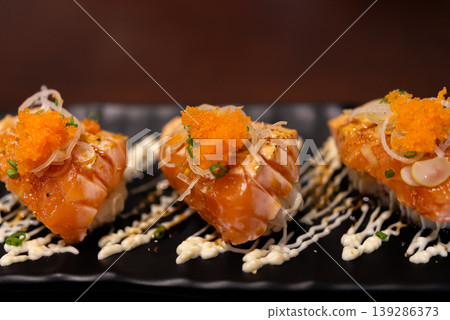 Close up salmon sushi bites topped with roe and sauce on black plate fresh seafood Japanese cuisine gourmet presentation rich flavor and texture ready to eat 139286373