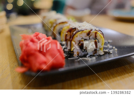 Several sushi rolls are presented next to pickled ginger on a dark plate Several sushi rolls are presented next to pickled ginger on a dark plate 139286382