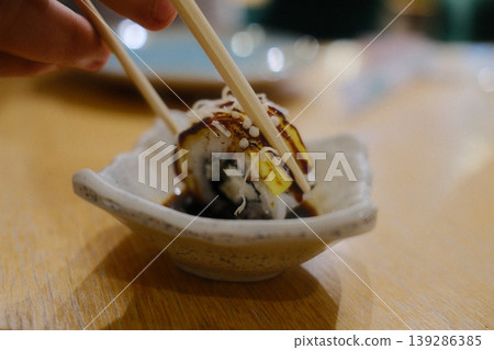 A sushi roll is lifted from sauce using chopsticks for dinner 139286385