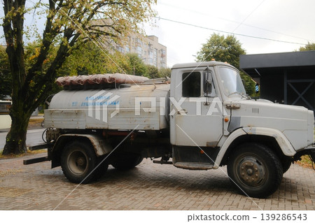 A weathered water tank truck, marked Lutskvodokanal, stands on a brick paved city street A weathered water tank truck, marked Lutskvodokanal, stands on a brick paved city street 139286543