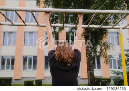 Person hangs from a metal bar. Building and tree are visible in the background 139286560