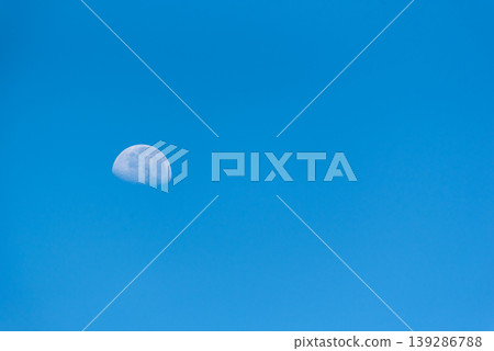 Half moon visible in bright blue sky during daytime minimal composition with large copy space calm atmosphere and natural light ideal for background or space concept Half moon visible in bright blue sky during daytime minimal composition with large copy space calm atmosphere and natural light ideal for background or space concept 139286788