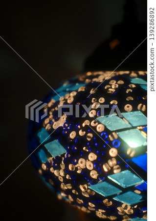 A colorful glass mosaic lamp emits light, revealing its intricate patterns in a dark interior 139286892