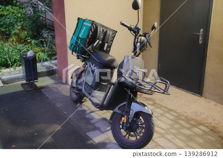 A food delivery moped with a bag sits parked on a paved street 139286912