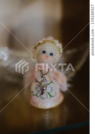 Small angel figurine holds a jeweled cross on a necklace in a display case 139286927