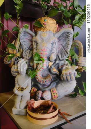 Ganesha and Buddha statues displayed, along with plants and a money offering Ganesha and Buddha statues displayed, along with plants and a money offering 139286936