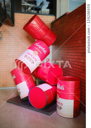 A stack of decorative Campbell's soup cans and red barrels appear indoors A stack of decorative Campbell's soup cans and red barrels appear indoors 139286939